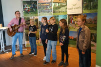 Person mit Gitarre und 5 Kinder auf einer Bühne